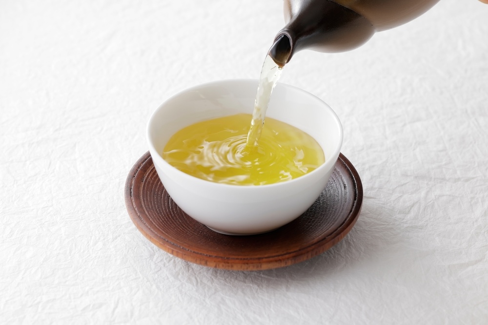 Green tea being poured from a traditional Japanese teapot into a white cup